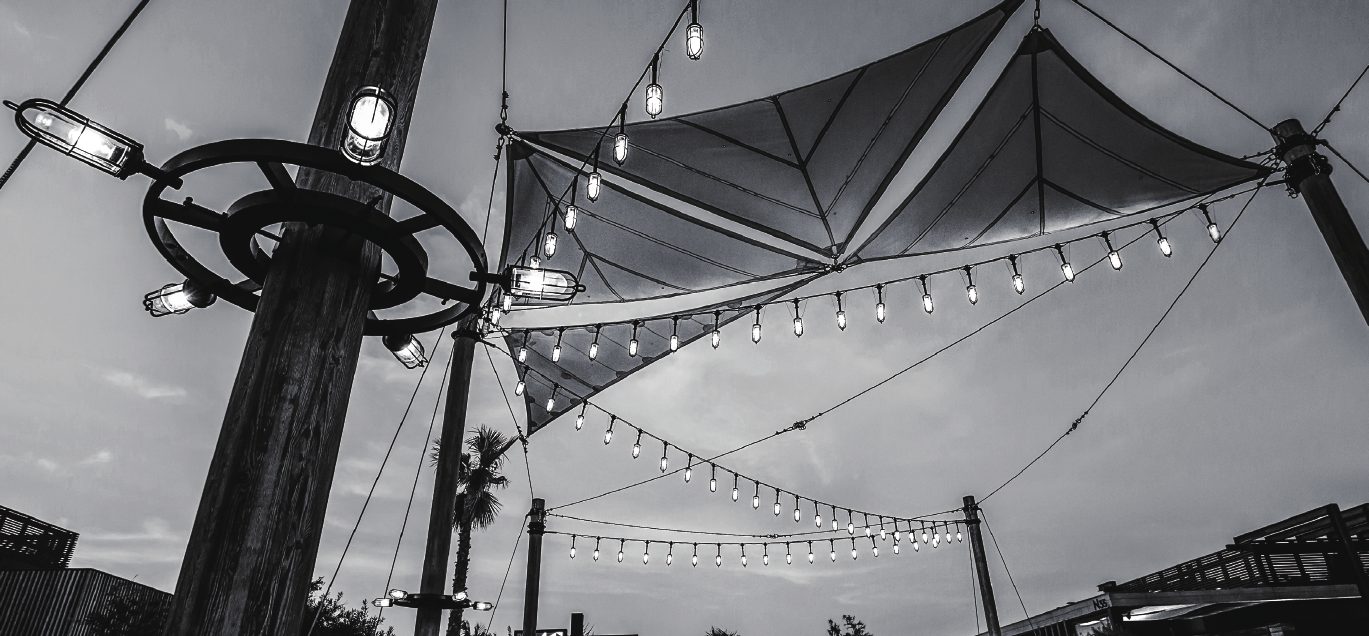 Festoon string-light installation beneath sail canopies — an outdoor lighting project by Dasher